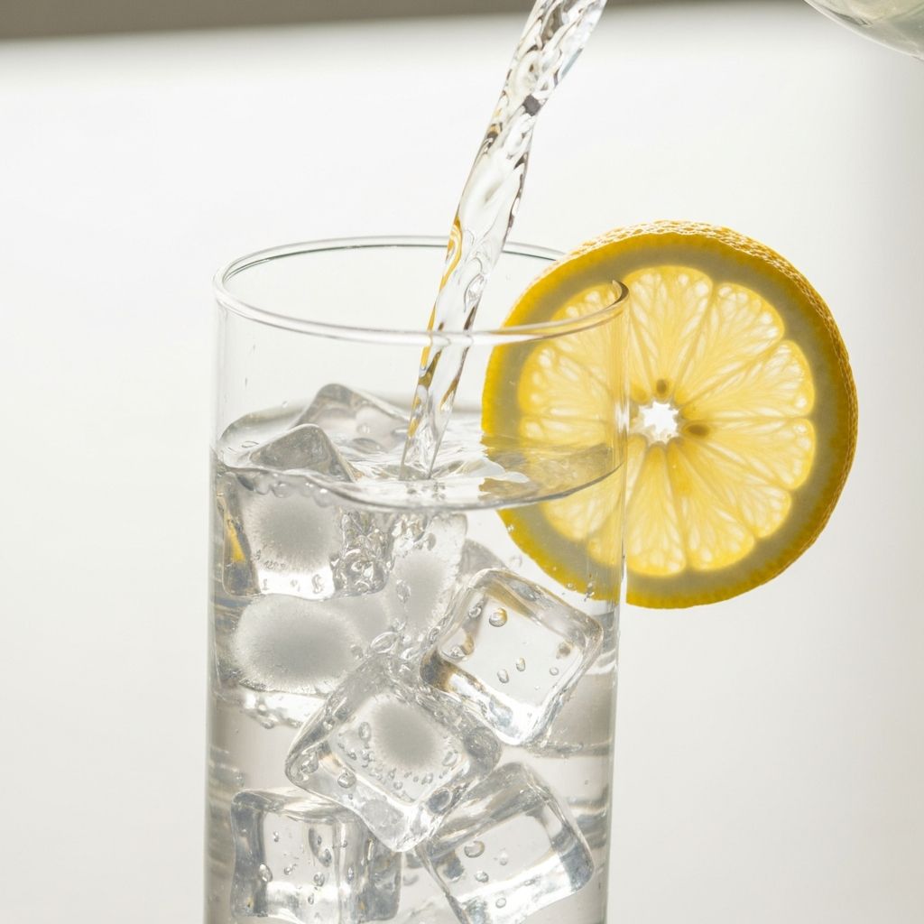 Clean water being poured into a glass with ice and fresh lemon slice, minimalist composition